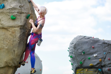 Photo of sporty blonde exercising on climbing boulder against sky with clouds