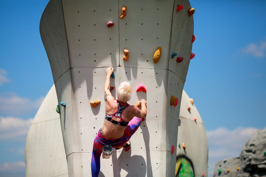 Photo from back of sports blonde in leggings on wall for rock climbing against blue sky
