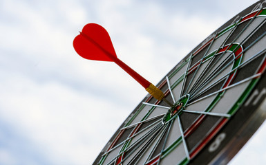 Red dart arrow hitting in the target center of dartboard marketing competition concept, on sky...