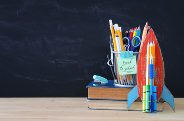 Back to school concept. cardboard rocket and pencils over open book in front of classroom blackboard.