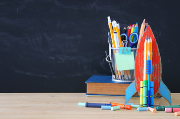 Back to school concept. cardboard rocket and pencils over open book in front of classroom blackboard.