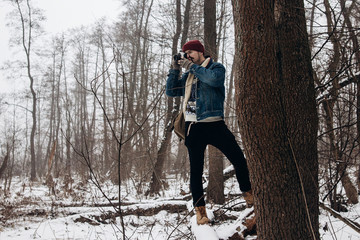 stylish hipster traveler holding camera and making photo in snowy forest. wanderlust and adventure concept with space for text. atmospheric moment