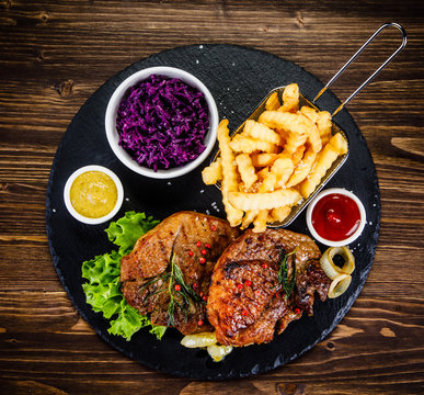 Grilled steak with french fries and vegetables served on black stone on wooden table