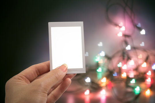 Hand holding instant photo or picture frame with blurred christmas lights background with copy space warm retro vintage tone.
