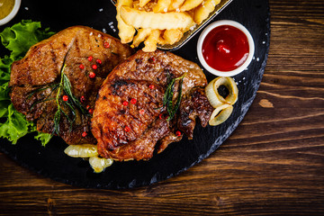Grilled steak with french fries and vegetables served on black stone on wooden table
