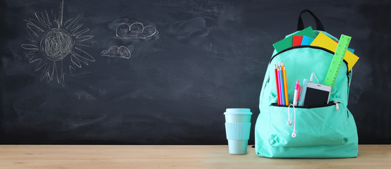 school bag with stationery and notebooks in front of blackboard. Back to school concept.