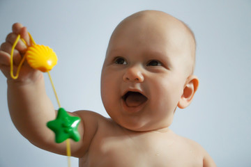 chest portrait of a laughing baby close-up, which is holding a colorful rattle on a uniform...