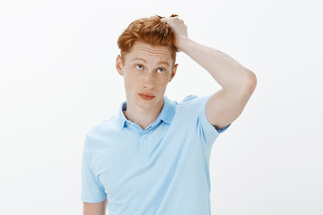 Handsome guy getting dressed for important meeting. Portrait of carefree good-looking redhead man touching hair with carefree casual expression, looking up, trying to look cool over gray background