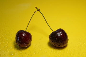 two cherry berries on a yellow background water drops