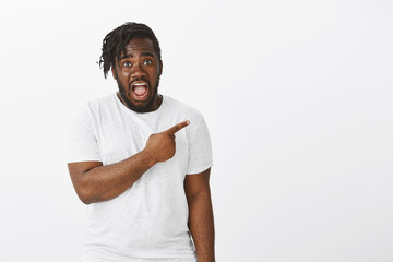 Omg, look. Portrait of shocked intense african-american male model with beard, pointing right, dropping jaw and gasping, seeing something stunning, standing speechless over white background