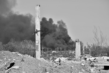 A pile of concrete rubble with protruding rebar on the background of thick black smoke in the blue sky. Black and white