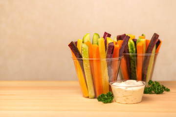 colorful carrots and cucumbers vegetables julienned in plastic cups and sour cream dip decorated parsley over wooden board