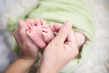 Close-up tiny baby feet in hands. Mother care of newborn baby.