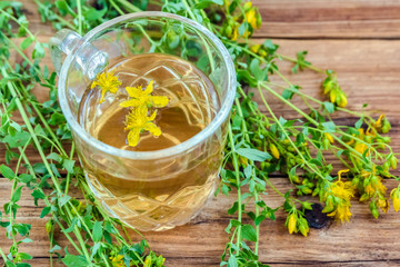 Cup of herbal tea from Hypericum - St. John's wort plant on wooden board table.