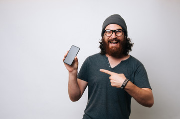 Amazed bearded man wearing eyeglasses and pointing at phone screen