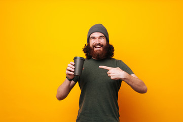Happy bearded man pointing at mug cup of coffee to go