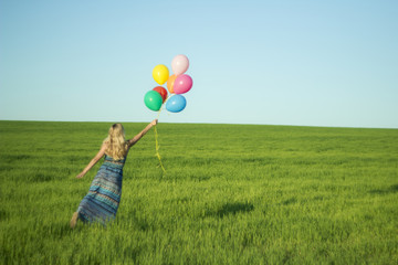 Girl with balloons in the field. Solar and positive energy of nature. Young beautiful woman on the grass in the Park.