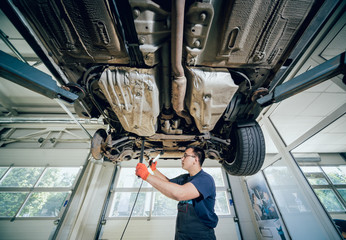 Car mechanic examining car suspension of lifted automobile at repair service station