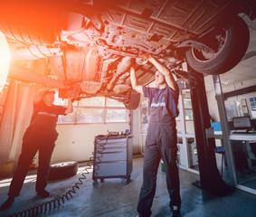 Car mechanics repair car suspension of lifted automobile at repair service station