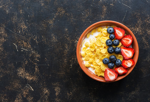 Breakfast corn flakes with milk and fresh berries, strawberries, blueberries on a dark background. Top view, copy space. Dietary food. Flat lay