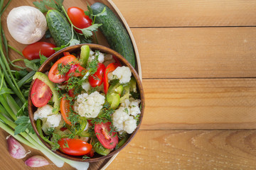 Fresh salad of cauliflower with tomatoes, broccoli, olives, sweet pepper, herbs and vegetables in a bowl on a wooden table. Top view. Copy space. Close-up