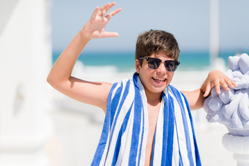 Young child on holidays wearing a navy towel by the beach very happy and excited, winner expression celebrating victory screaming with big smile and raised hands