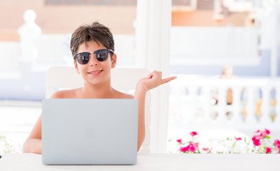 Young child on holidays using computer laptop very happy pointing with hand and finger to the side