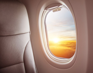 Airplane interior with window view of sunset above clouds.