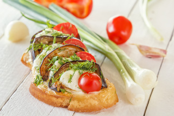 Bruschetta with fried eggplants, fresh tomatoes and cheese on white boards against the background of fresh vegetables. Close-up