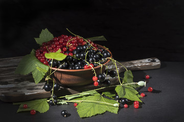 Black and red currants in a clay cup on a dark background.
