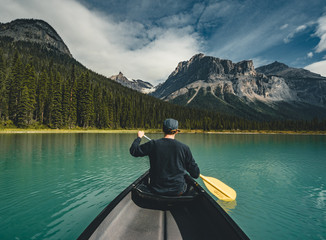 Young Man Canoeing on Emerald Lake in the rocky mountains canada with canoe and mountains in the background blue water.