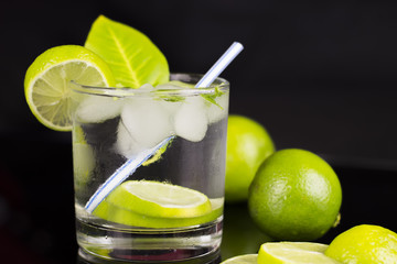 Alcohol drink (Gin Tonic cocktail) with lime and ice on black background with reflections