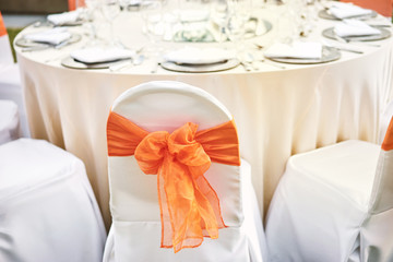 Back of spandex white cover chairs orange organza sash for wedding reception dinner table