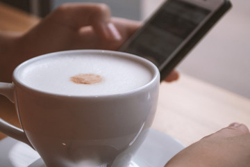 A cup of coffee and a smartphone in the girl's hand