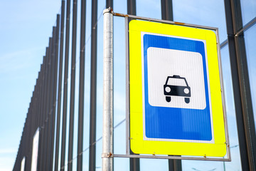 Taxi sign against a modern building and blue sky.