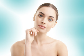 Obraz na płótnie Canvas Portrait of a beautiful young woman with naked shoulders smiling while posing at isolated light blue background. Face beauty skin care. Natural make up