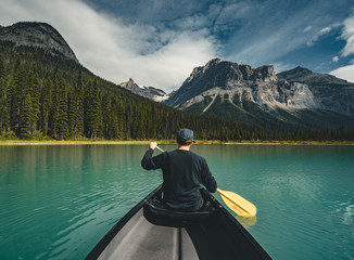 Young Man Canoeing on Emerald Lake in the rocky mountains canada with canoe and mountains in the...