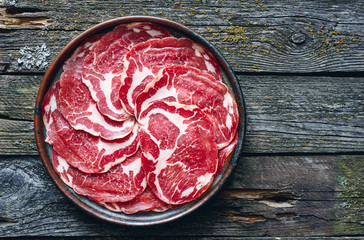 Delicious Italian smoked meat in plate on wooden table top view 