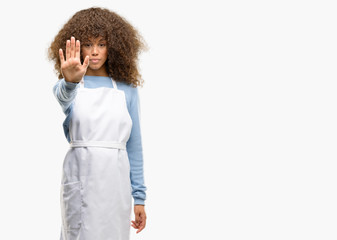 African american shop owner woman wearing an apron annoyed with bad attitude making stop sign with hand, saying no, expressing security, defense or restriction, maybe pushing