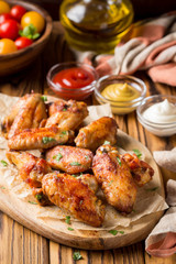 Grilled chicken wings with ketchup and mustard sauces on wooden board. Traditional baked bbq buffalo