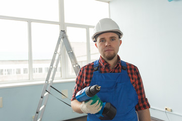 Happy white male builder with screwdriver infront of ladder, wearing white helmet.