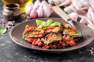 Fried eggplant slices with tomatoes, herbs and garlic, tasty vegetarian summer lunch. Grilled aubergine