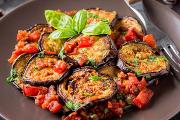 Fried eggplant slices with tomatoes, herbs and garlic, tasty vegetarian summer lunch. Grilled aubergine