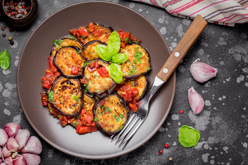 Fried eggplant slices with tomatoes, herbs and garlic, tasty vegetarian summer lunch. Grilled aubergine