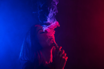 Young woman in neon light and smoke of e-cigarettes or vape on dark background