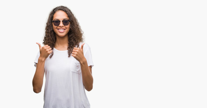 Young hispanic woman wearing sunglasses success sign doing positive gesture with hand, thumbs up smiling and happy. Looking at the camera with cheerful expression, winner gesture.