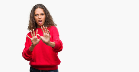 Fototapeta premium Young hispanic woman wearing red sweater afraid and terrified with fear expression stop gesture with hands, shouting in shock. Panic concept.