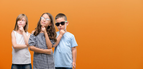 Group of boy and girls kids over orange background serious face thinking about question, very...