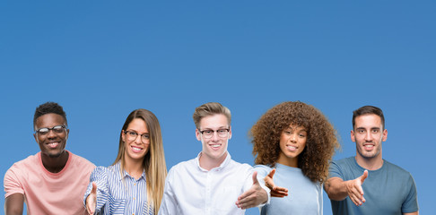 Composition of group of friends over blue blackground smiling friendly offering handshake as greeting and welcoming. Successful business.