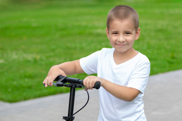 Obraz premium Portrait of a child outdoors. A happy boy is riding a scooter